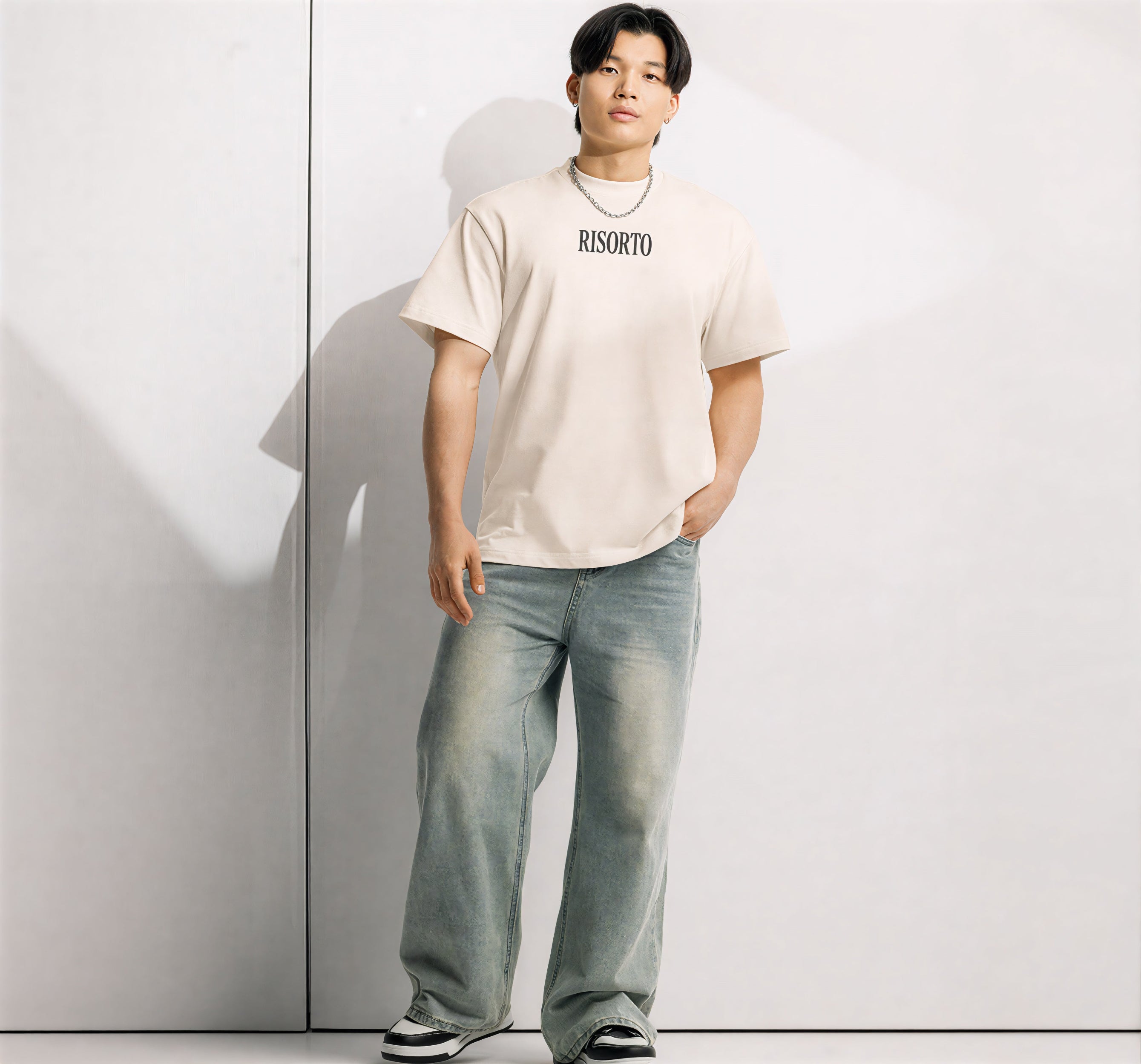 Person wearing a beige t-shirt with 'RISORTO' logo and light blue jeans against a white background